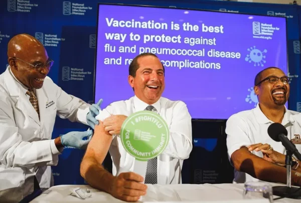 Picture showing a case of vaccination from one person to another, including a banner supporting vaccination in the background. 