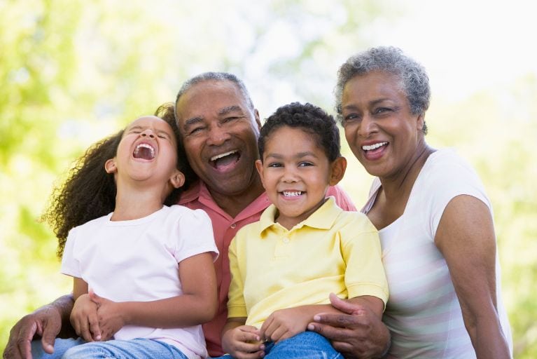 2 black grandparents hugging younger children